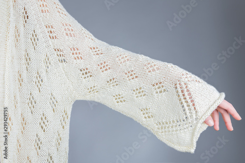 Female hand in a beige cardigan on a gray background. Long sleeve