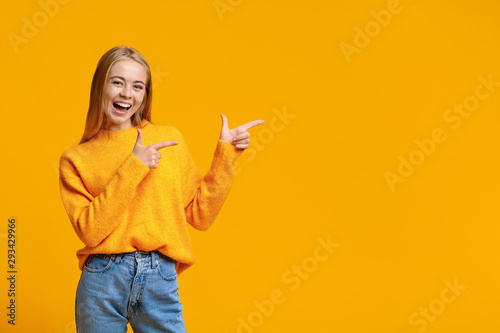 Bild auf Leinwand Cheerful teenage girl pointing at copy space on orange background