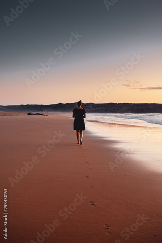 Silhouette of a girl in colorful sunset gradient at a peaceful beach on a tropical beach. Praia da Bordeira at the Algarve Coast in Portugal, Atlantic Ocean
