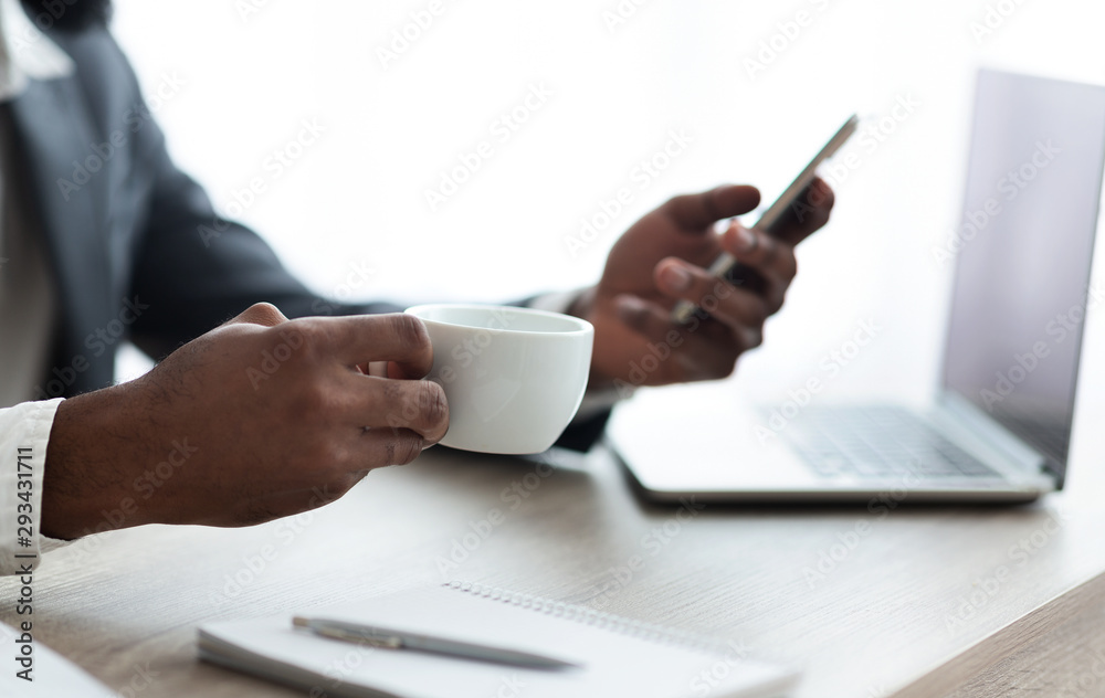 Black businessman drinking coffee and using smartphone at workplace Black businessman drinking coffee and using smartphone at workplace