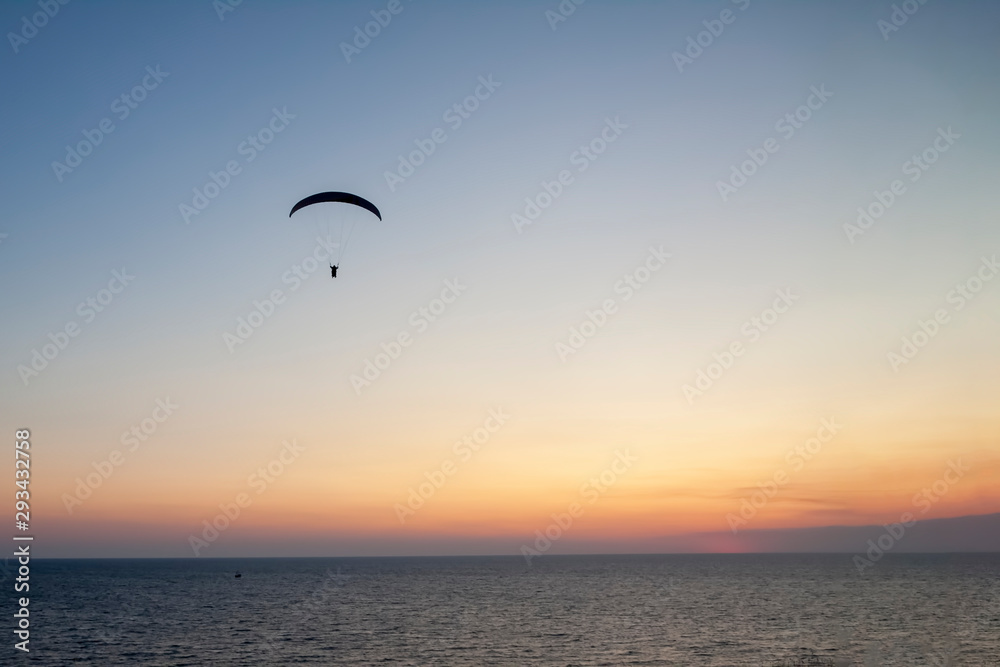 Paraglider with a man high in the blue sky against the setting sun.