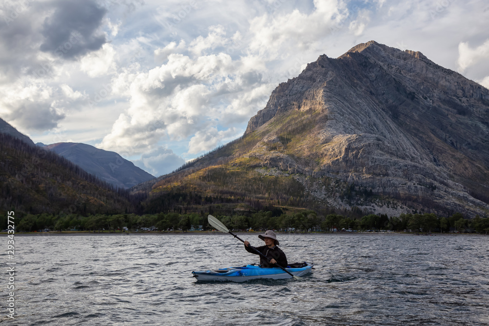 Adventurous Man Kayaking in Glacier Lake surrounded by the beautiful Canadian Rocky Mountains during a cloudy summer sunset. Taken in Upper Waterton Lake, Alberta, Canada. Adventurous Man Kayaking in Glacier Lake surrounded by the beautiful Canadian Rocky Mountains during a cloudy summer sunset. Taken in Upper Waterton Lake, Alberta, Canada.