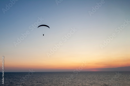 Paraglider with a man high in the blue sky against the setting sun.