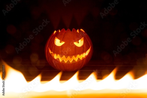 Spooky carved halloween pumpkin in hot burning hell fire flames. Big helloween autumn symbol with mad face, glowing eyes, mouth and teeth. Scary hot nightmare horror with evil smile at october 31st