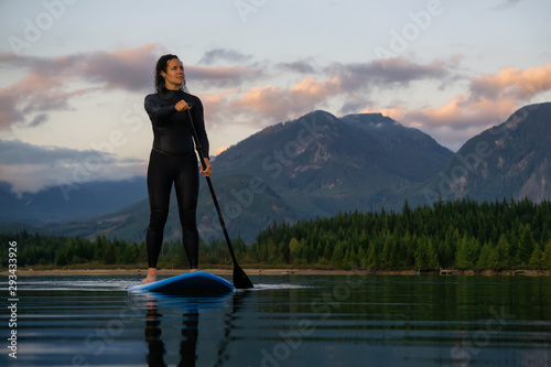 Adventurous Girl on a Paddle Board is paddling in a calm lake with mountains in the background during a colorful summer sunset. Taken in Stave Lake near Vancouver, BC, Canada.