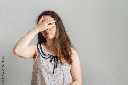 Emotions and people. A young brunette in a blouse covered her eyes with her hand and Peeps through it. Emotion of secrecy and curiosity. Copy space