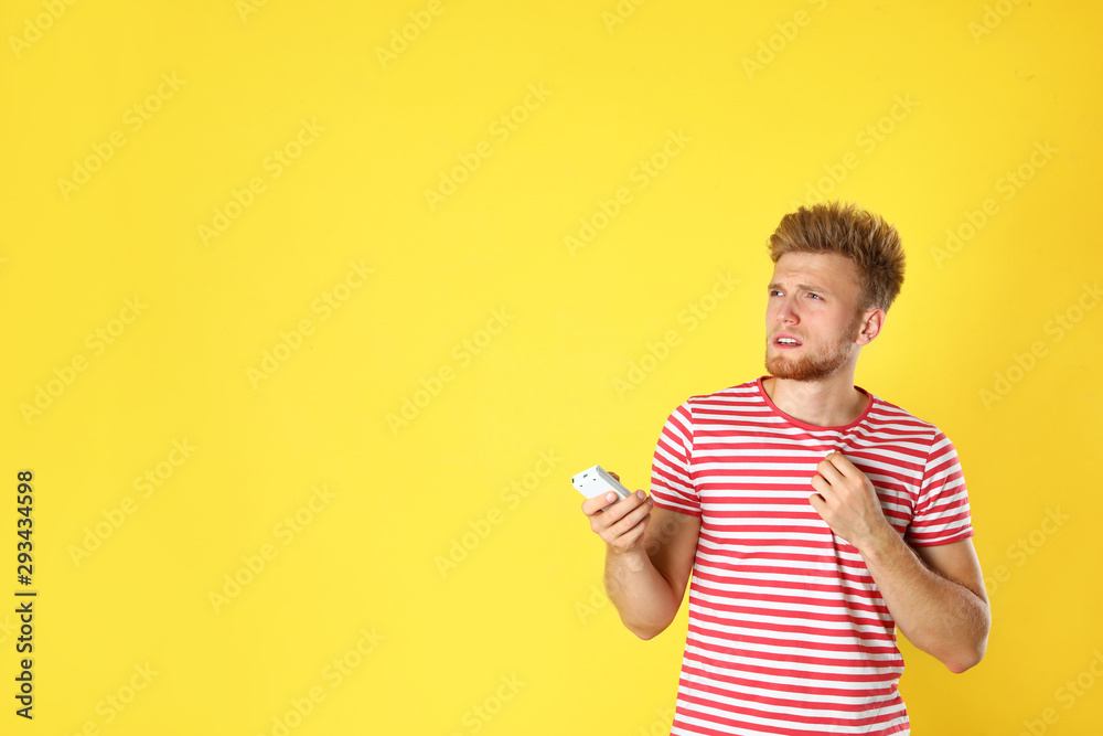 Young man with air conditioner remote suffering from heat on yellow background. Space for text Young man with air conditioner remote suffering from heat on yellow background. Space for text