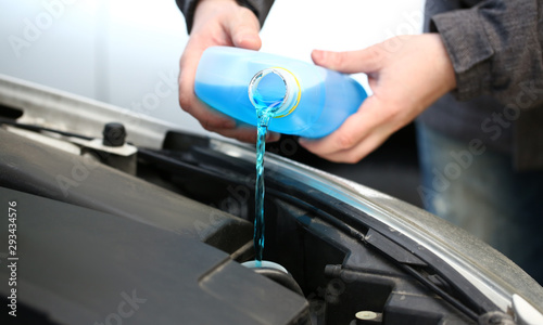 Canvas Print Male serviceman hands pouring blue washer fluid from a bottle into car concept