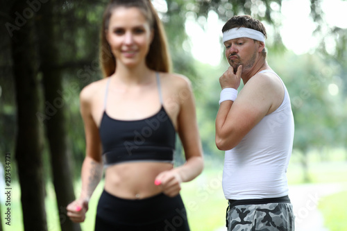Fototapeta Naklejka Na Ścianę i Meble - Obese man doing morning jogging in park. A girl with great figure runs by. The guy turns around look and surprisingly evaluates quality of body. Wow girls meme concept