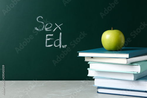 Books and apple on grey table near chalkboard with phrase 