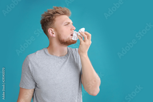 Young man suffering from allergy on blue background. Space for text