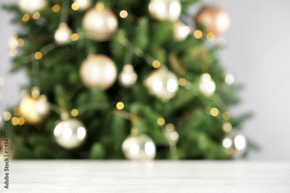 Empty white wooden table and blurred fir tree with Christmas lights on background, bokeh effect. Space for design