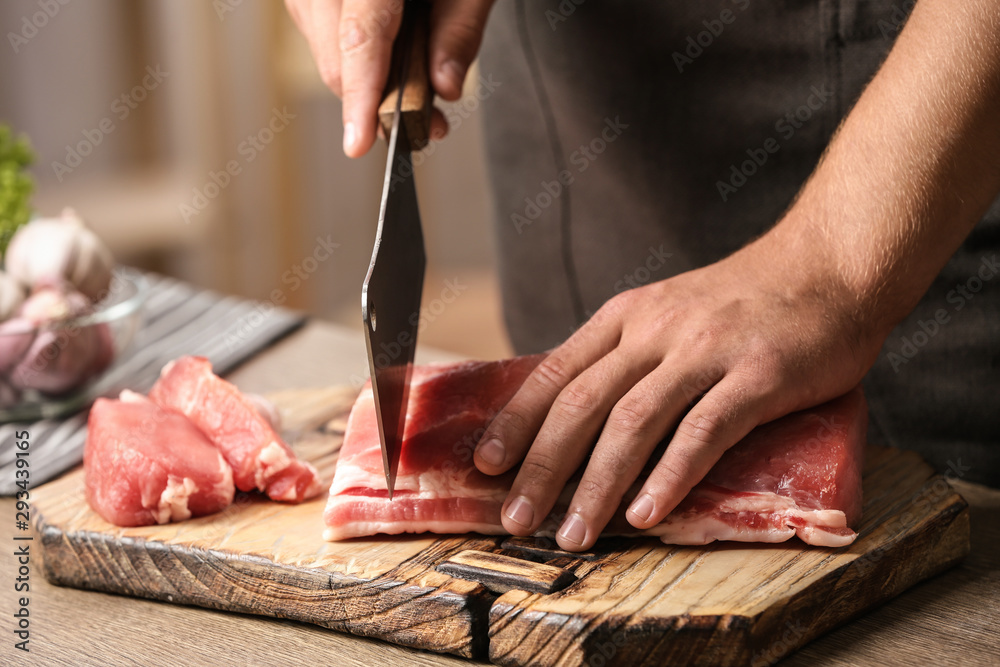 Man cutting fresh raw meat on table in kitchen, closeup - obrazy, fototapety, plakaty 