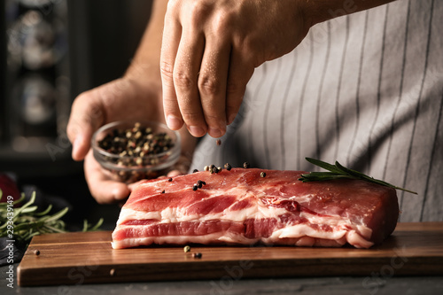 Fotografie Man cooking fresh raw meat with pepper and rosemary on table, closeup