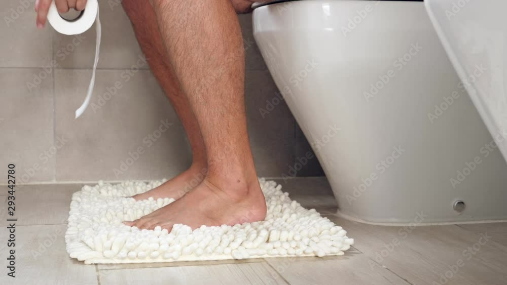 Man sitting on wc toilet bowl at the bathroom and holding a toilet paper roll, no face