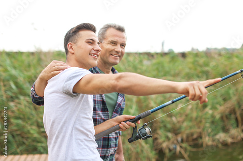 Young man and his father fishing on river