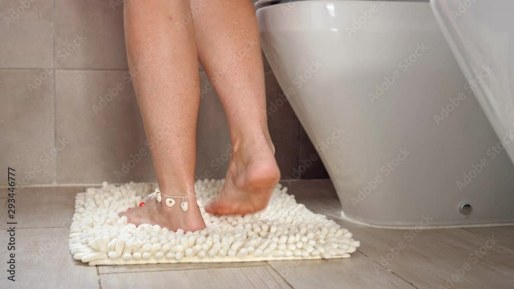 Woman sitting on wc toilet bowl at the bathroom and taking a toilet paper roll, no face