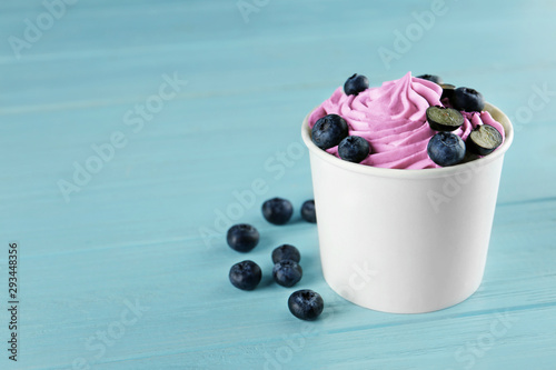 Cup with tasty frozen yogurt and blueberries on blue wooden table. Space for text photo