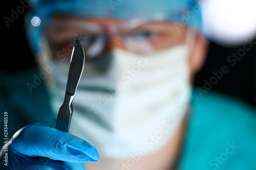 Surgeon arms in sterile uniform holding sharp knife while operating patient in surgical theatre closeup. Stop bleeding put stitch innovation er 911 team cancer tumour concept photo