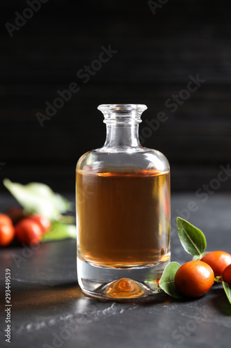 Glass bottle with jojoba oil and seeds on grey stone table against dark background