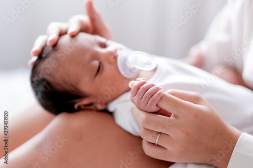 Newborn baby with teat was put on her mother knees who sit on bed and also take care with love.