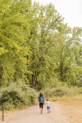 A woman and a child hiking, walking along a dirt path.