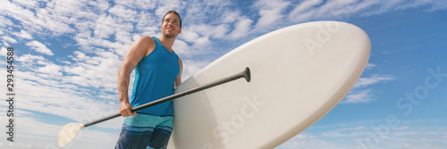 Paddle board SUP fit man carrying paddleboard on hawaii beach banner panorama. Fitness active lifestyle fun activity outdoors athlete. photo