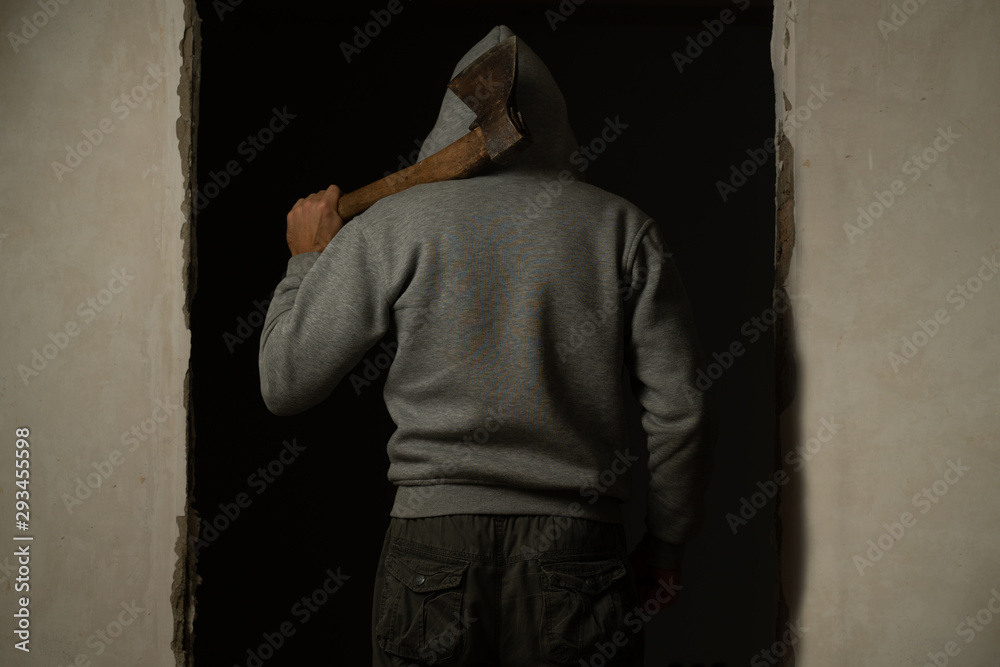 A hooded man with an axe on his shoulder rear view A hooded man with an axe on his shoulder rear view