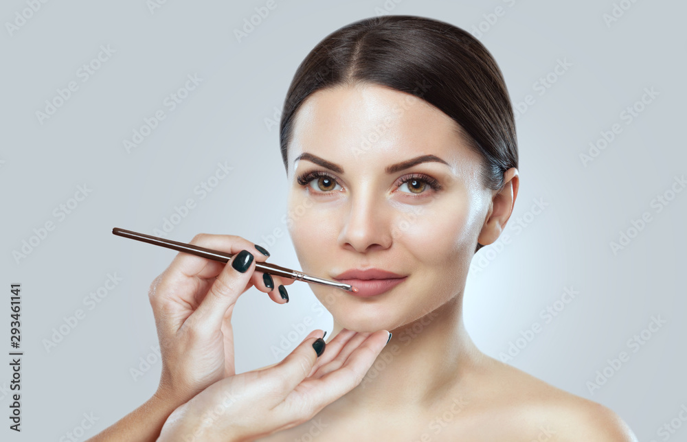 Fototapeta premium The make-up artist paints the lips of a beautiful woman, completes the make-up in the beauty salon. Professional skin care.