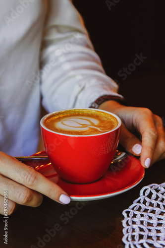 Hands of a young woman take a red ceramic coffee cup on a wooden brown table. Conceptual for the holiday Halloween.
