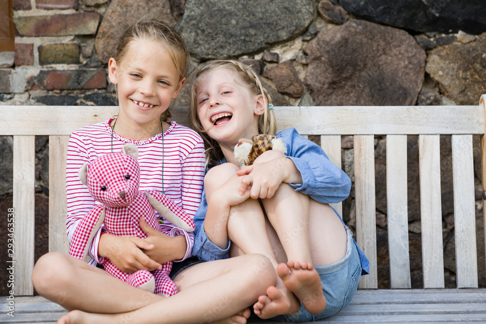 © Westend61 - Portrait of two happy girls sitting on a bench with their soft toys