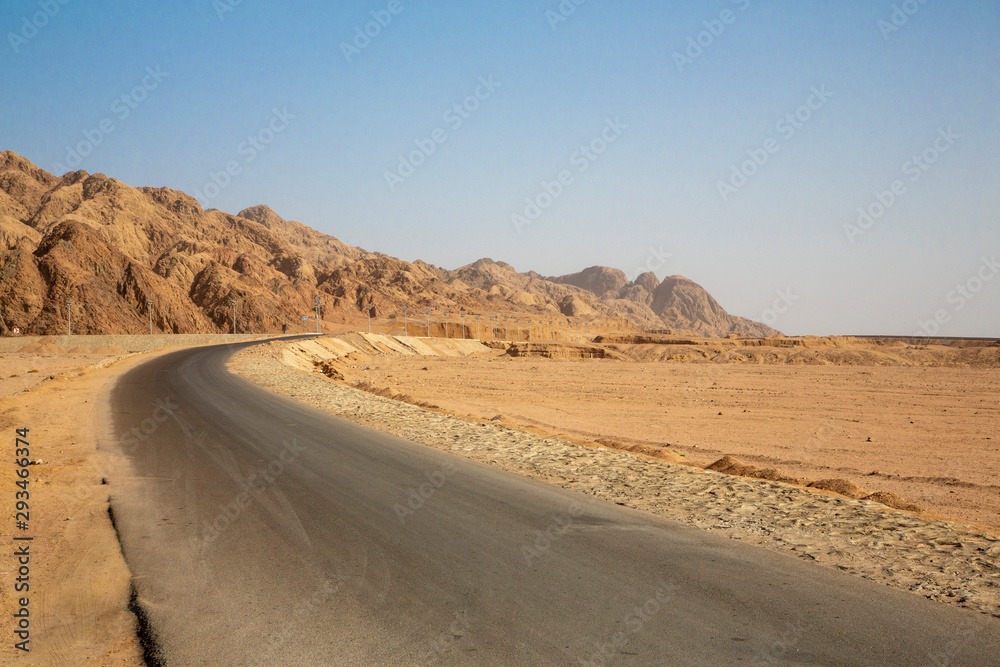 Empty road by rock formation in desert against clear blue sky Empty road by rock formation in desert against clear blue sky