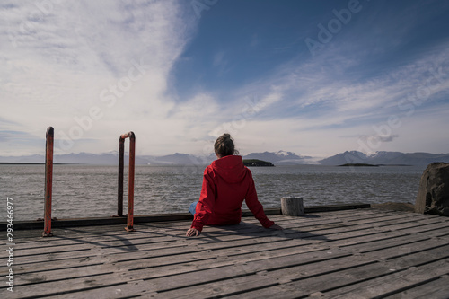 Young woman sitting on a jetty, looking at the sea, South East Iceland