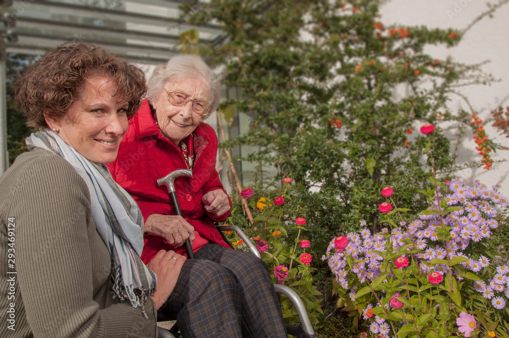 Obraz premium Smiling senior woman with wheelchair and young woman in the garden