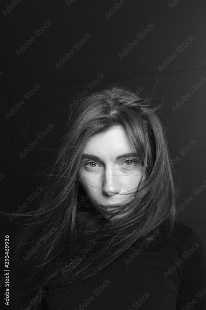 Black and white portrait of a beautiful girl with hair flying in the wind on a dark background Black and white portrait of a beautiful girl with hair flying in the wind on a dark background