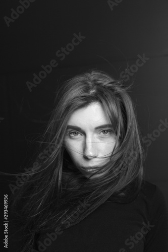 Black and white portrait of a beautiful girl with hair flying in the wind on a dark background