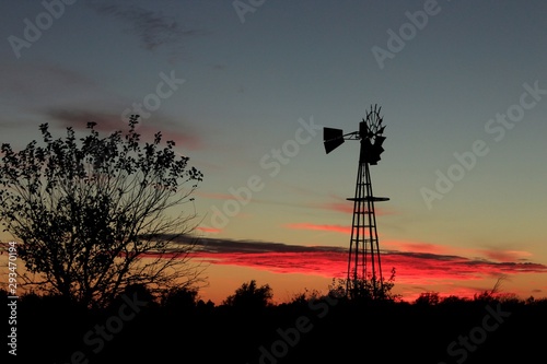 Windmill at sunset with red cloud's and tree's in Kansas