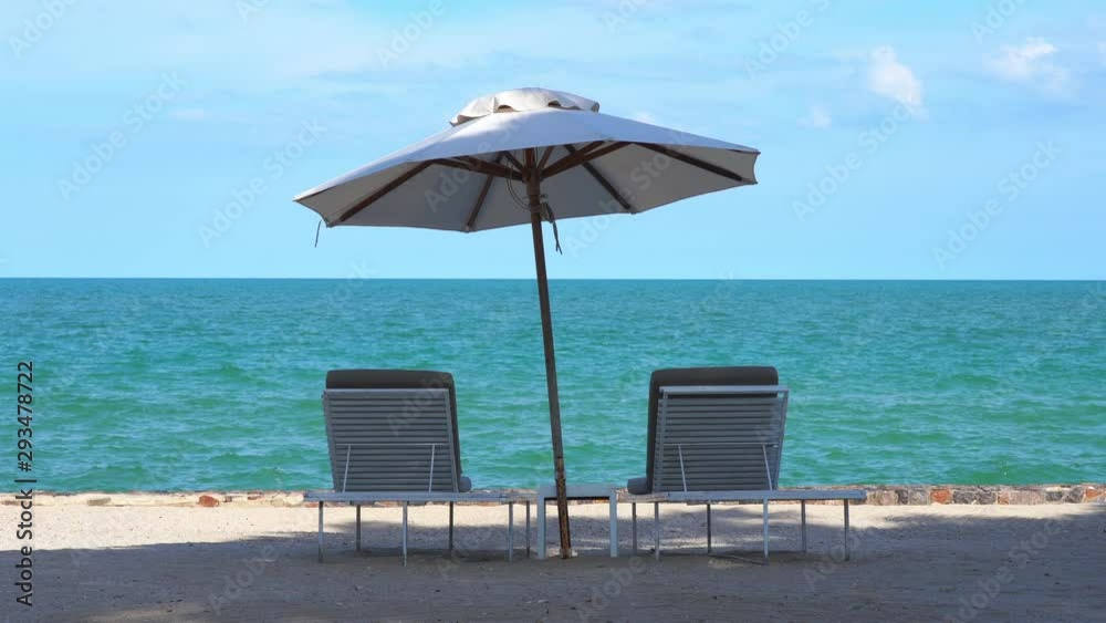 Two empty resort sun loungers sit under a shade umbrella on a white sand beach facing the ocean horizon.