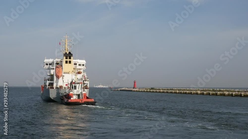 Container Cargo Ship with Auxiliary Boat goes out from port to the sea at summer day