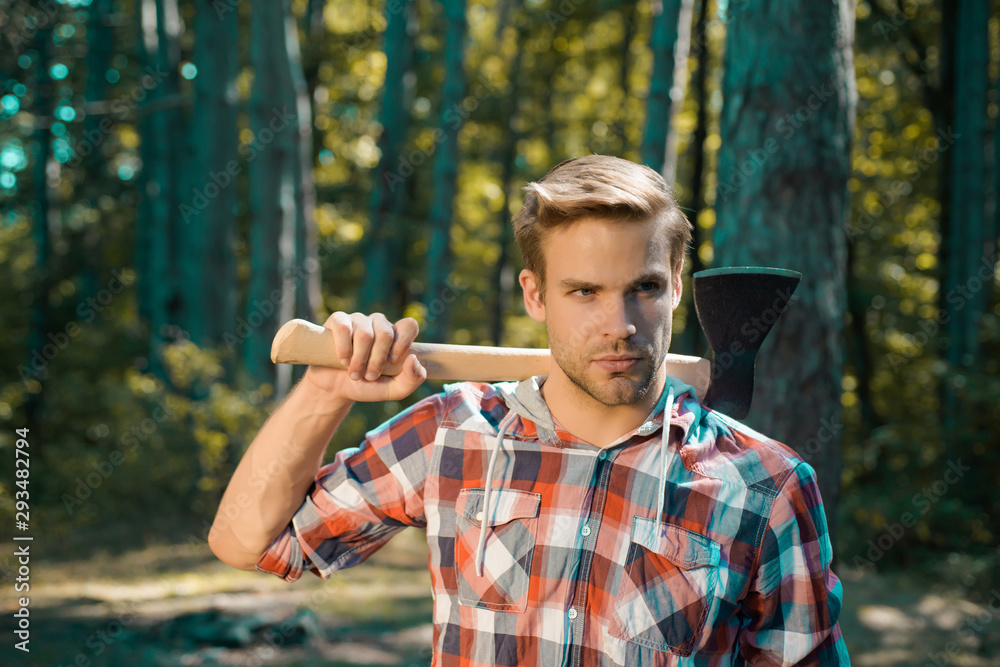 Obraz premium Lumberjack on serious face carries axe on shoulder. Bearded man with axe concept. Lumberjack with axe on forest background. Man doing mans job. Harvest of timber.