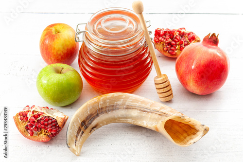 Happy Rosh Hashanah, judaism, traditional autumn holiday in jewish culture and judaic new year conceptual idea with ram horn or shofar, jar of honey, apple and pomegranate isolated on wood background