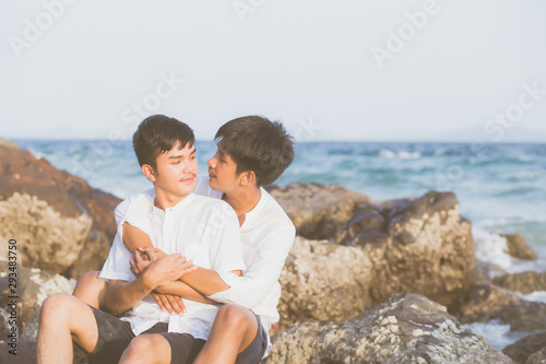 Homosexual portrait young asian couple sitting hug together on rock or stone in the beach in summer  asia gay going tourism for leisure and relax with happy in vacation at sea  LGBT legal concept.