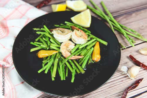 Fried asparagus shrimp prawns cooking food on wooden plate and fresh asparagus bunch on the table