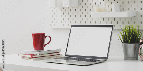 Comfortable workplace with open blank screen laptop computer with red coffee cup and office supplies