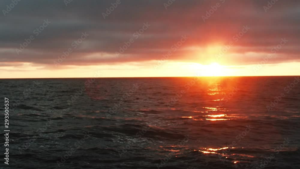Bright red golden sun sets below horizon. Light reflects on ocean coastline. Bright red golden sun sets below horizon. Light reflects on ocean coastline.
