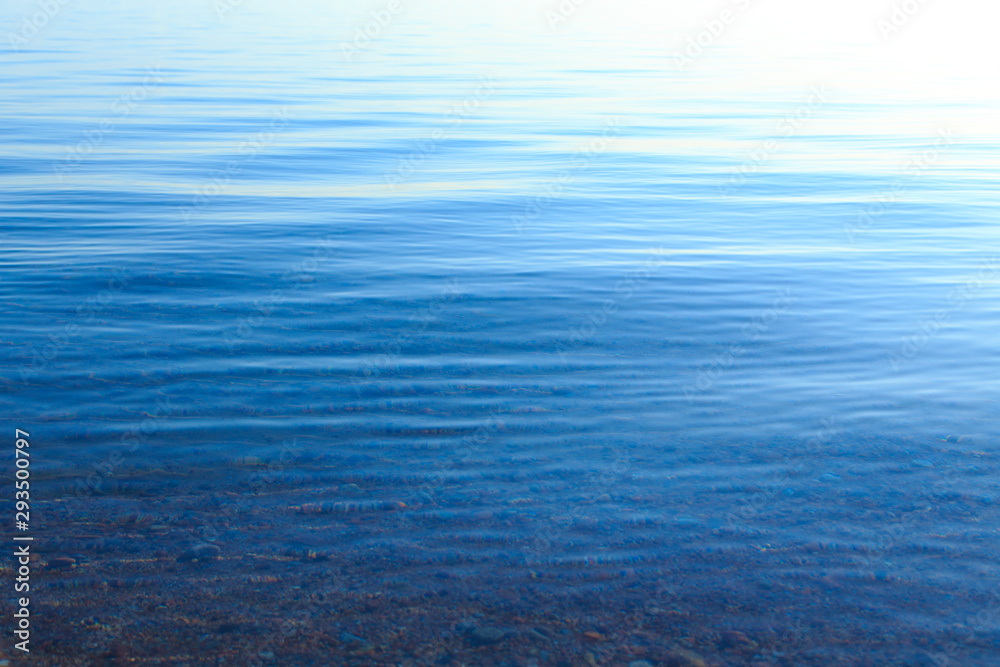 Clear water texture in blue and orange. Background of the ocean and the sea backlit by the sun. Soft waves. Natural water Clear water texture in blue and orange. Background of the ocean and the sea backlit by the sun. Soft waves. Natural water