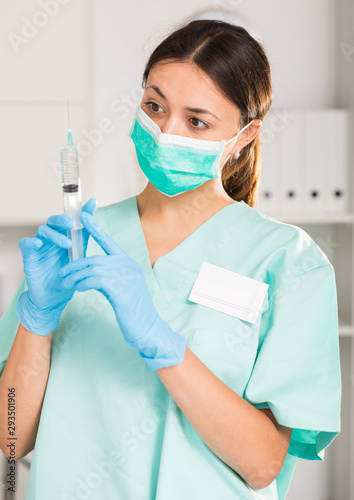 Female nurse in mask holding syringe for injection in hospital