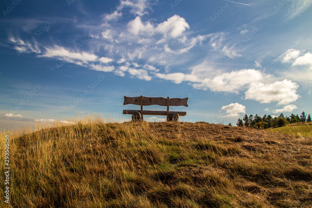 Holzbank auf einem Hügel unter weissem Wolken und blauem Himmel Holzbank auf einem Hügel unter weissem Wolken und blauem Himmel