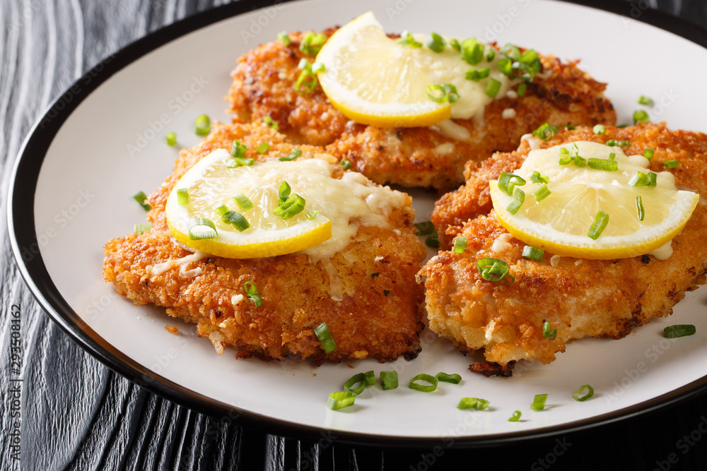 Romano cheese chicken cutlet fried breaded served with lemon and green onion closeup on a plate. horizontal