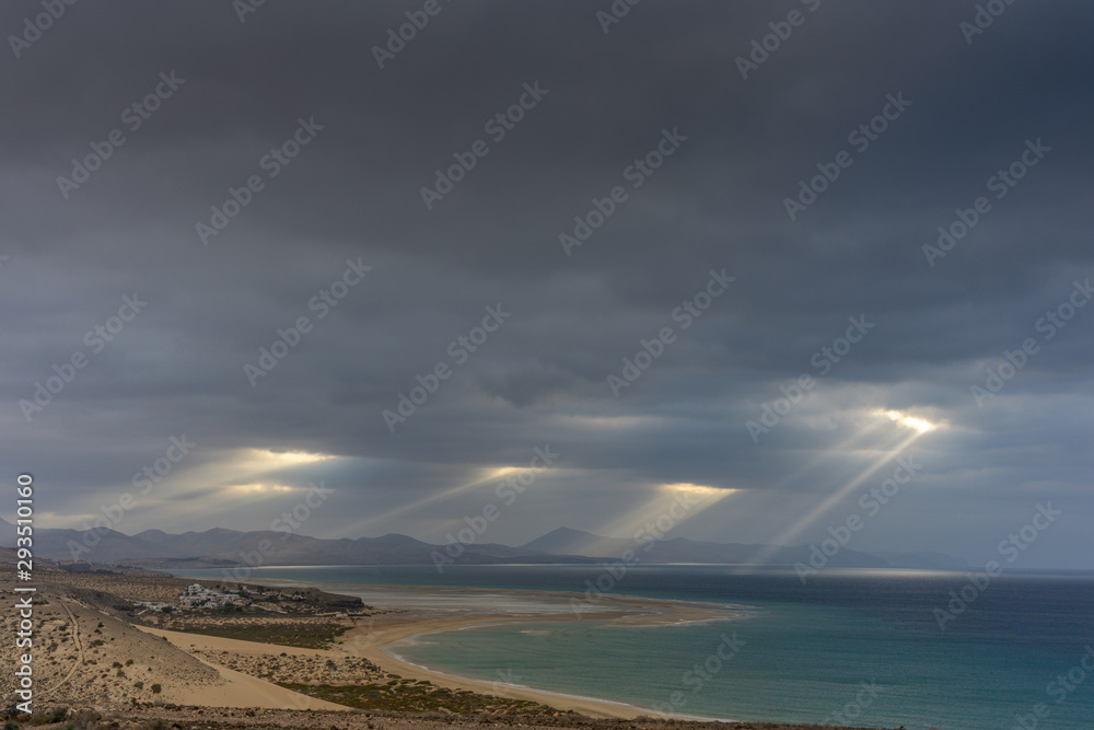 View in the morning on the coast of Risco del Paso on Fuerteventura with sunbeams and dark clouds
